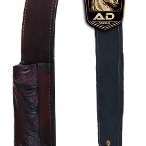 Puede incluir: Una cincha de silla de montar de caballo de cuero marrón oscuro con un diseño decorativo tallado. La cincha tiene una hebilla de metal y una anilla en D. El logotipo "AD Saddler" es visible.