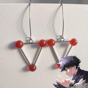 May include: A pair of silver-toned earrings featuring a geometric design. Each earring has a triangular shape with three red, spherical beads at the corners and a long, curved hook for the ear.
