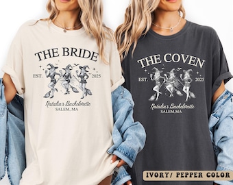 May include: Two t-shirts, one ivory and one pepper color, featuring a witch-themed design. The ivory shirt reads "THE BRIDE" with "Natalia's Bachelorette, Salem, MA" and the year 2025. The pepper color shirt says "THE COVEN" with the same details.