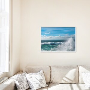 Pode incluir: Uma fotografia de uma grande onda quebrando na costa. A água é de um azul e verde vibrantes, e o céu é de um azul claro com nuvens brancas. A onda quebra em uma espuma branca, e o sol brilha intensamente.