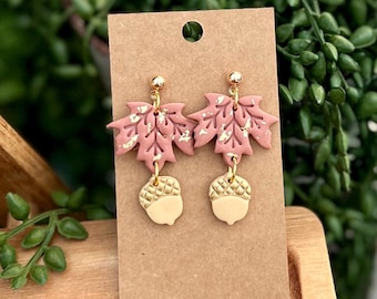 May include: A pair of dangle earrings featuring pink maple leaf charms with gold accents and gold acorn charms.