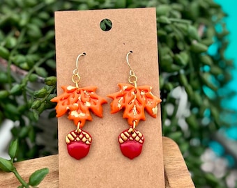 May include: A pair of dangle earrings featuring orange and gold leaf charms with red acorn accents.