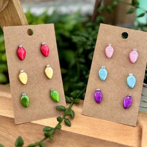 May include: Two sets of Christmas light bulb stud earrings in various colors, including red, yellow, green, pink, blue, and purple. The earrings are displayed on brown cardboard earring cards.