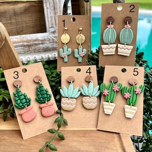 May include: A collection of handmade polymer clay earrings featuring cactus and succulent designs. The earrings are displayed on brown cardstock with wooden stud tops. The earrings come in various colors, including green, pink, and beige, and are designed to resemble potted plants.