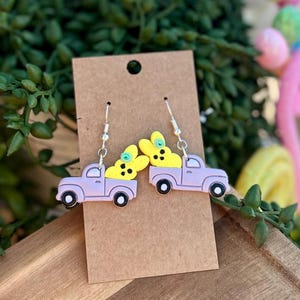 May include: Purple truck earrings with yellow bunny peeps in the bed of the truck. The earrings are on a brown card.