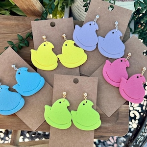 May include: Assortment of colorful pastel-colored marshmallow-shaped earrings. The earrings are made of polymer clay and feature a variety of colors, including pink, blue, yellow, and green.