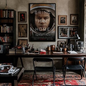 May include: A framed movie poster for The Martian featuring a close-up of a person in a space helmet with the text BRING HIM HOME. The poster is displayed on a wall above a dark wooden desk with two black chairs and a red and blue patterned rug.