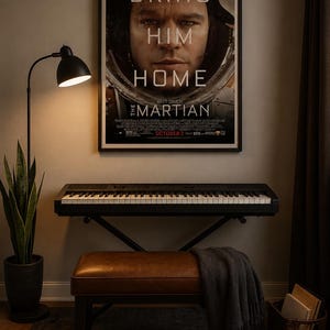 May include: A framed movie poster for The Martian featuring Matt Damon in a space helmet with the text BRING HIM HOME, positioned above a black electronic keyboard on a stand, a brown leather bench with a gray throw, and a floor lamp.