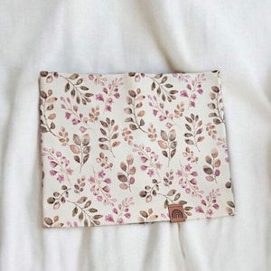Könnte beinhalten: Ein weißer Stoff-Halswärmer mit einem Blumenmuster aus braunen Blättern und rosa Blüten. Der Stoff hat einen dezenten Aquarell-Effekt.