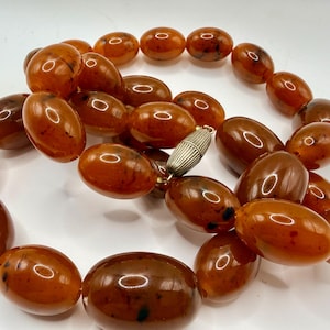 May include: A vintage amber necklace with large, oval beads in shades of brown and orange. The beads are strung together with a silver-coloured clasp. A striking piece of jewellery.