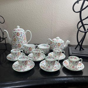 May include: A floral tea set comprising a teapot, creamer, sugar bowl, and six teacups and saucers. The set features a delicate floral pattern in shades of pink, yellow, green, and blue.