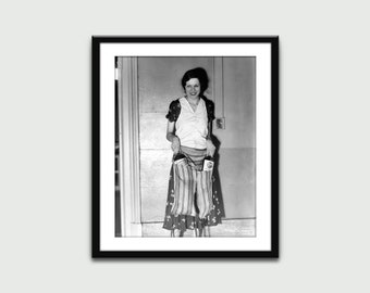 Può includere: Una fotografia in bianco e nero di una donna in piedi in una porta. Sta sorridendo e tiene due borse nelle sue mani. Le borse sono a righe e hanno un motivo floreale. La donna indossa una blusa bianca e una gonna.