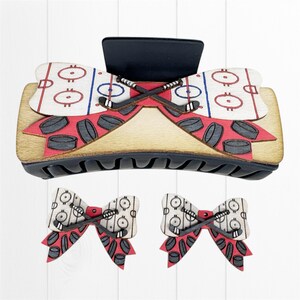 Könnte beinhalten: Eine Haarspange aus Holz und zwei passende ohrringförmige Schleifen. Die Spange und die Ohrringe haben ein Hockey-Thema mit Eisbahndesign, Hockeyschlägern und Pucks. Die Spange ist etwa 10 cm lang.