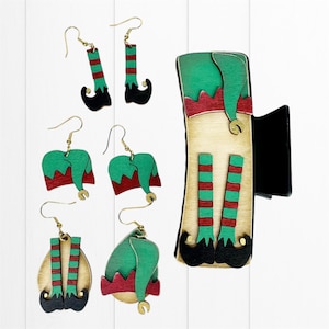 May include: Set of elf-themed earrings and a hair clip. The earrings feature green hats, red and white striped legs, and black shoes. The hair clip features a full elf figure with a green hat, red and white striped legs, and black shoes.