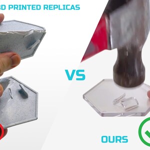 May include: A comparison of two hexagonal objects. The object on the left is a 3D printed replica that is cracked and broken. The object on the right is a clear, durable object that is being hit with a hammer. The text "3D PRINTED REPLICAS" is at the top left of the image. The text "VS" is in the middle of the image. The text "OURS" is at the bottom right of the image. A red X is next to the broken object. A green checkmark is next to the durable object.