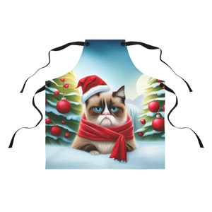 May include: A Christmas-themed kitchen apron featuring a grumpy cat wearing a Santa hat and a red scarf. The cat is surrounded by snow and Christmas trees with red ornaments.