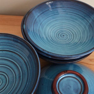 May include: A set of three ceramic bowls featuring a vibrant blue glaze with a prominent spiral pattern etched into the interior surface. The bowls have a smooth, glossy finish and a dark brown, unglazed circular base visible on the inverted bowl.