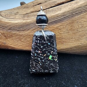 May include: Black opal pendant with silver wire wrapping and a black bead. The opal has a textured surface with iridescent flecks of color.