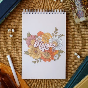 May include: A spiral bound notebook with a floral design and the word "Notes" in a retro font. The flowers are yellow, orange, pink, and white.