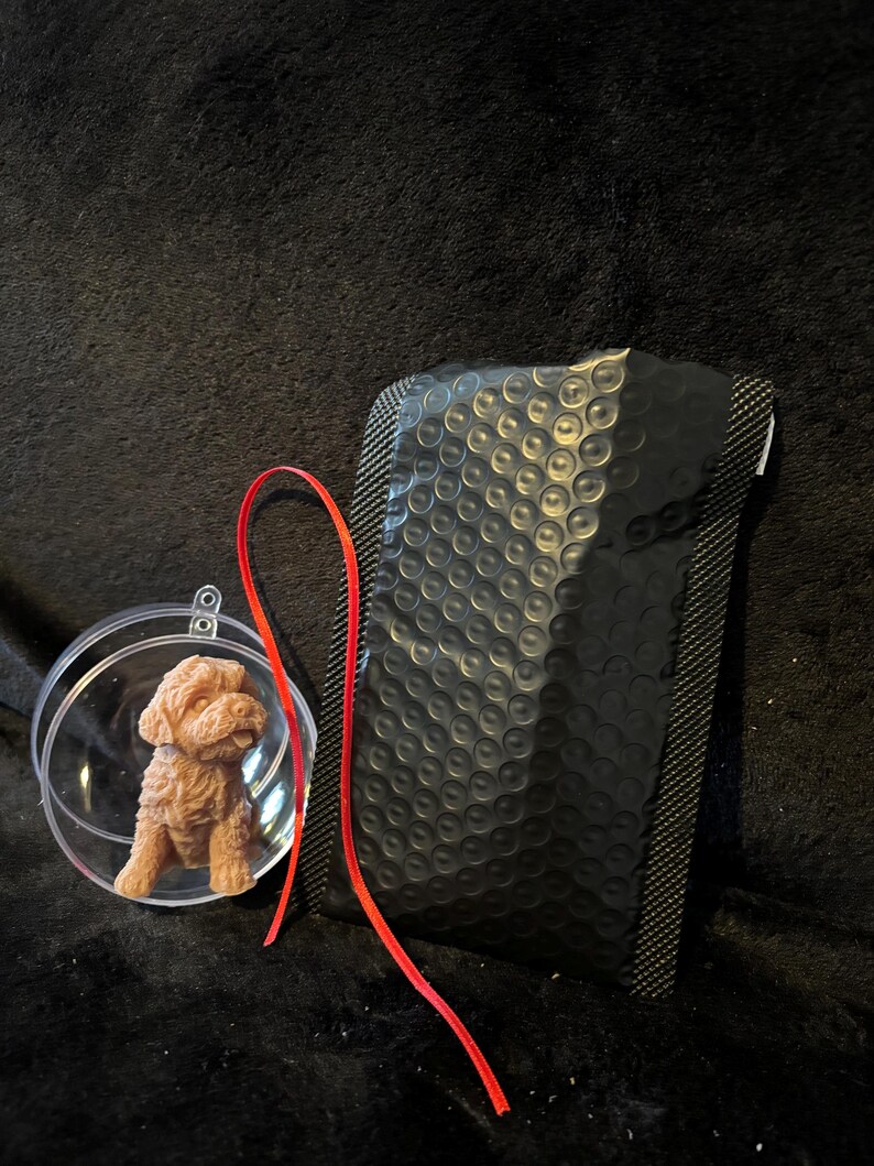 K&ouml;nnte beinhalten: Eine kleine, braune Hundefigur in einem durchsichtigen Glasornament mit einem roten Band.