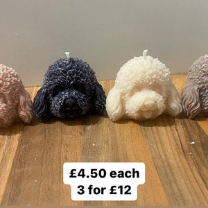 Puede incluir: Cuatro velas en forma de cabeza de caniche, hechas a mano. Las velas son de color rosa, negro, blanco y marrón. Las velas están sobre una superficie de madera. El texto "£4.50 each 3 for £12" está debajo de las velas.