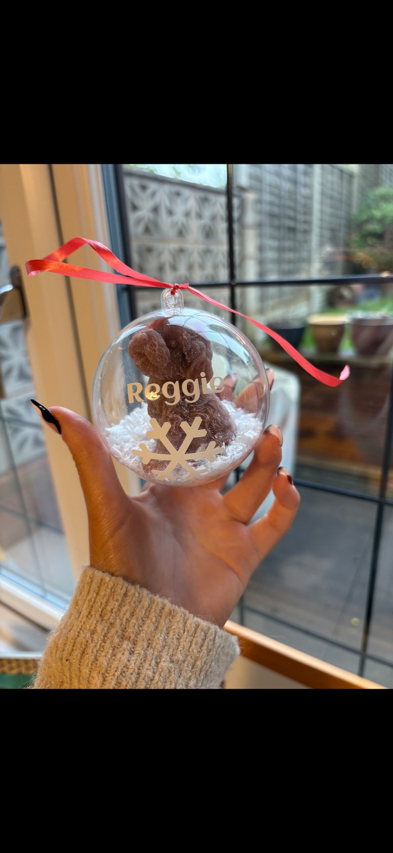 K&ouml;nnte beinhalten: Ein transparenter Weihnachtsbaumschmuck aus Glas mit einem braunen Pfotenabdruck im Inneren. Der Schmuck ist mit wei&szlig;em Glitzer gef&uuml;llt und hat ein rotes Band. Der Schmuck ist mit dem Namen "Reggie" und einer Schneeflocke personalisiert.