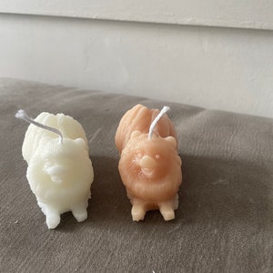 May include: Two small dog-shaped candles, one white and one light brown, with a white wick sticking out of the top of each candle.