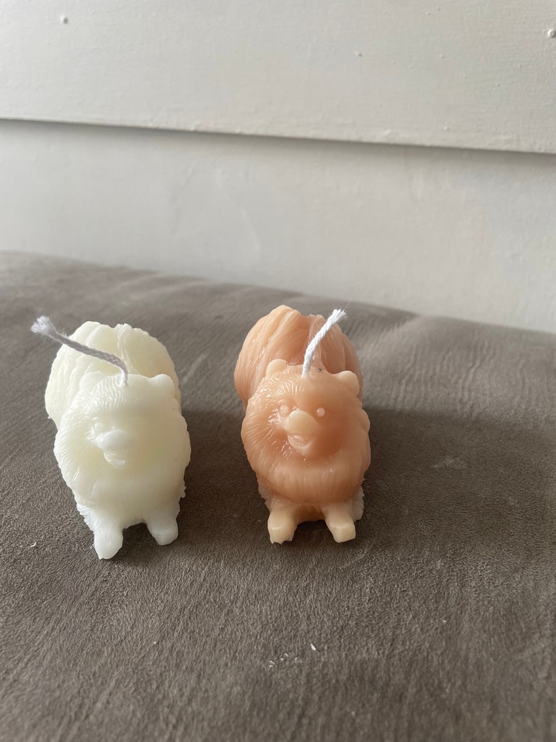 May include: Two small dog-shaped candles, one white and one light brown, with a white wick sticking out of the top of each candle.