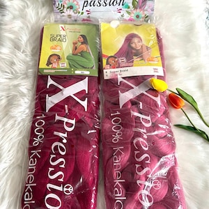 Puede incluir: Dos paquetes de cabello sintético trenzado de color burdeos, etiquetados como "X-Pression Super Braid 100% Kanekalon". El embalaje presenta imágenes de mujeres con peinados trenzados. Un letrero decorativo arriba dice "Elna's passion."