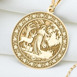 May include: A gold necklace with a round pendant featuring a detailed image of a woman standing in a forest with a deer. The pendant is surrounded by a decorative border of leaves.