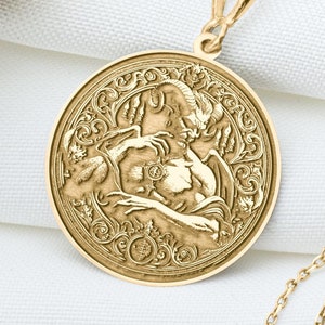 May include: Gold pendant necklace with a round, detailed medallion featuring a sculpted image of two figures embracing. The chain is a delicate, gold, box chain.