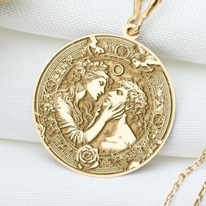 May include: A gold necklace with a round pendant featuring an embossed image of two figures embracing. The pendant is surrounded by a decorative border with floral motifs.