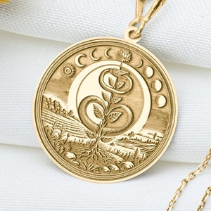 May include: Gold necklace with a round pendant featuring a detailed design of a plant growing between two crescent moons. The pendant is surrounded by a circle of smaller moons.