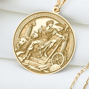 Könnte beinhalten: Eine goldfarbene Halskette mit Anhänger, die ein detailliertes Relief einer Wagenszene mit einem Löwen zeigt. Der Anhänger hängt an einer zarten Kette. Getrocknete Blumen sind im Hintergrund.