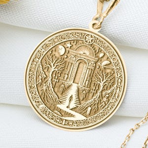 Może przedstawiać: Złoty naszyjnik z okrągłym wisiorem przedstawiającym skomplikowany wzór budynku ze ścieżką prowadzącą do niego, otoczonego drzewami i księżycem.
