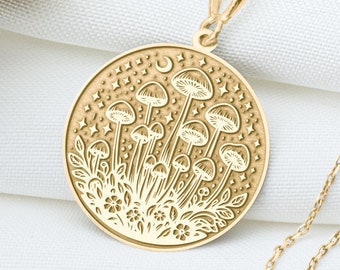 May include: A gold necklace with a round pendant featuring an engraved design of mushrooms and a crescent moon. The pendant is surrounded by small stars.