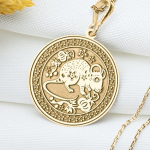 May include: Gold necklace with a round pendant featuring a detailed engraving of a rat. The pendant is surrounded by a decorative border.