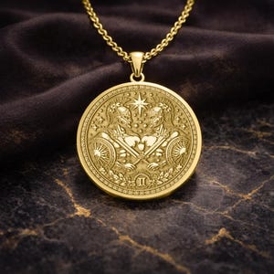 May include: A gold-colored pendant necklace featuring a circular medallion with a detailed relief design. The medallion depicts two figures in helmets, holding swords and shields, with a star and the Roman numeral II. The chain is also gold-colored.