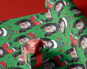 May include: Green wrapping paper with a repeating pattern of Christmas trees, Santa hats, and faces. The faces are of different people, and the paper is wrapped around a small gift box with a red ribbon.