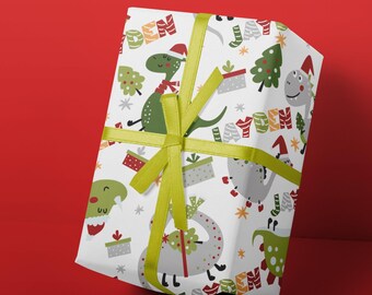 May include: White wrapping paper with a repeating pattern of green and gray dinosaurs wearing Santa hats, Christmas trees, and the name "Layden" in red and green letters. The paper is tied with a green ribbon.