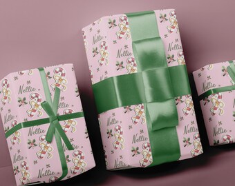 May include: Three wrapped gifts with pink wrapping paper featuring a pattern of candy canes, gingerbread people, and the name "Nellie." The gifts are tied with green satin ribbon and bows, creating a festive holiday presentation.