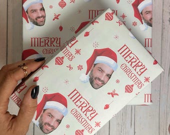 May include: Wrapping paper with a repeating pattern of a smiling face wearing a Santa hat, snowflakes, and the words "MERRY CHRISTMAS" in red. The background is a light green color.