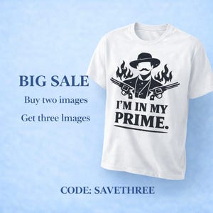 May include: White t-shirt with a black graphic of a mustached man in a hat, two guns, and flames. Text on the shirt reads "I'M IN MY PRIME." The shirt is on a light blue background.