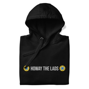 Pode incluir: Camisola de capuz preta com o texto "Howay the Lads" e duas estrelas amarelas com centros azuis.