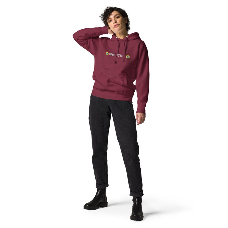 Puede incluir: Una sudadera con capucha color granate con un gr&aacute;fico blanco que dice "DON'T BE LAZY" y dos caritas sonrientes amarillas. La modelo lleva pantalones vaqueros negros y botas negras.