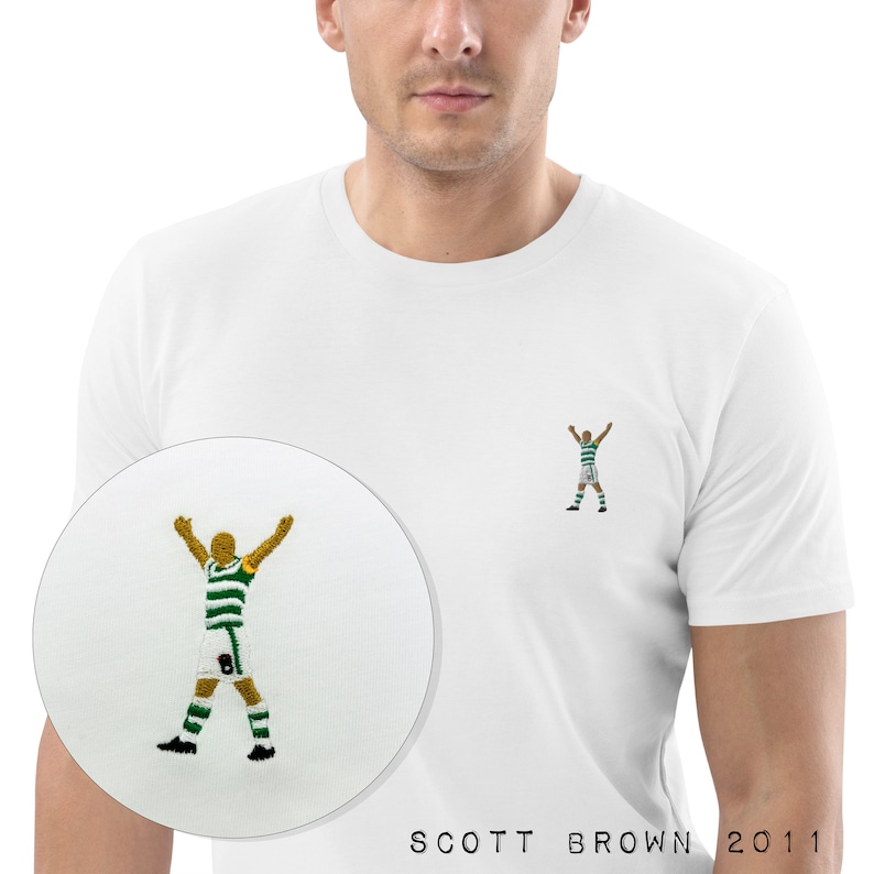 May include: White t-shirt with an embroidered image of a soccer player celebrating a goal. The text "SCOTT BROWN 2011" is printed on the bottom of the shirt.