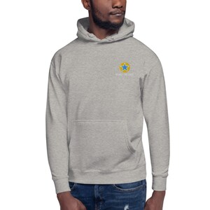 K&ouml;nnte beinhalten: Ein grauer Kapuzenpullover mit einem gelben Kreis und einem blauen Stern auf der Vorderseite. Der Text "NORTH THE EDGE" ist in Wei&szlig; unter dem Stern geschrieben.