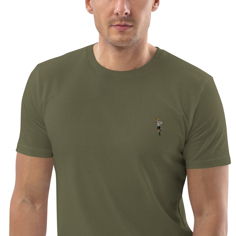 May include: A green t-shirt with a small embroidered image of a referee holding a yellow card.