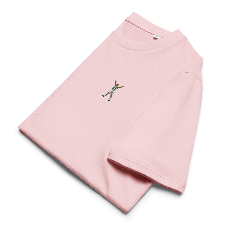 May include: A pink t-shirt with a small embroidered image of a soccer player celebrating a goal.
