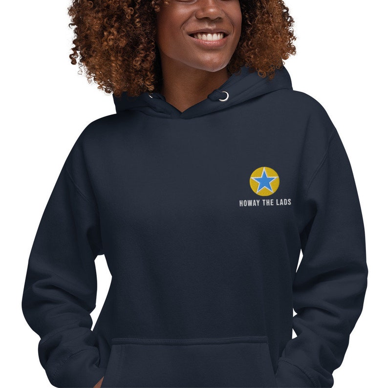 K&ouml;nnte beinhalten: Ein marineblauer Hoodie mit einem gelben Stern- und blauen Stern-Design und dem Text "Howay the Lads", der auf der Vorderseite gestickt ist.